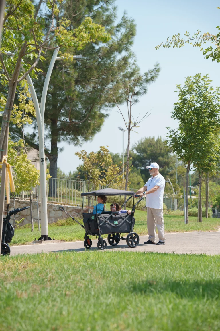 סבא מטייל עם שתי ילדים שיושבים בתוך עגלת היקדו וואגן רקע פארק